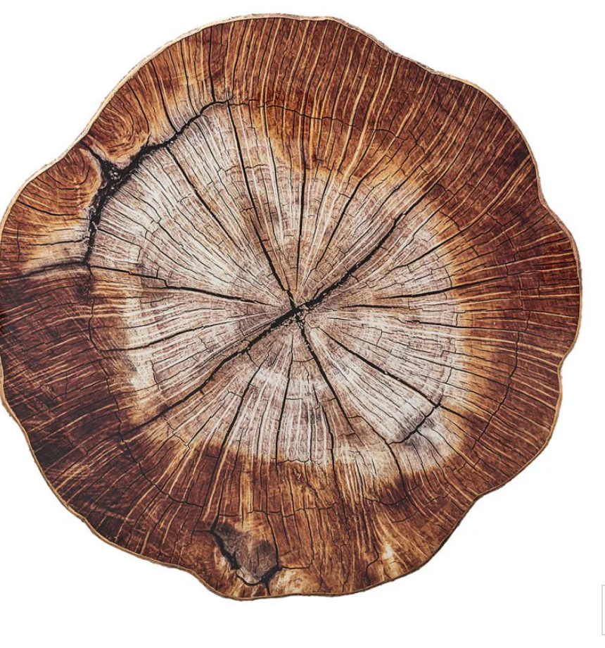 The Cedar Placemat by Kim Seybert features a cross-section tree trunk design with growth rings and natural wood texture, making it an ideal rustic accent or inspiration for wood-slice placemats.