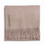 Alicia Adams Alpaca's Classic Throw, a folded beige blanket from the Alicia Adams Alpaca collection, is crafted from cashmere and baby alpaca, featuring fringes on the bottom edge and a small fabric tag on the left side. It is fair-trade made in Peru.