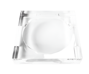 The Lucite Tray Small by L'Avant Collective features a clear, square design with a large central circular indent, highlighting minimalist style. Photographed against a white background.