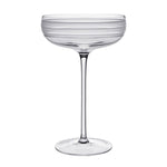 The Madison Drinkware Collection by William Yeoward Crystal features a clear coupe with a tall stem and horizontal frosted stripes, evoking Jazz Age elegance, shown here against a white background.