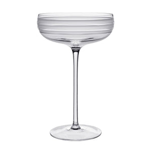 The Madison Drinkware Collection by William Yeoward Crystal features a clear coupe with a tall stem and horizontal frosted stripes, evoking Jazz Age elegance, shown here against a white background.
