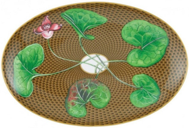 The Tresor Fleuri Marron Dinnerware Collection by Raynaud features an oval plate with a woven brown pattern, five hand-painted green leaves connected by stems, and a pink flower, radiating poetic porcelain charm.