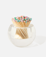 The Acrylic Match Striker Collection by Tart by Taylor features a clear round glass container filled with wooden matches tipped in pastel colors—a stylish, functional accessory perfect for your coffee table.
