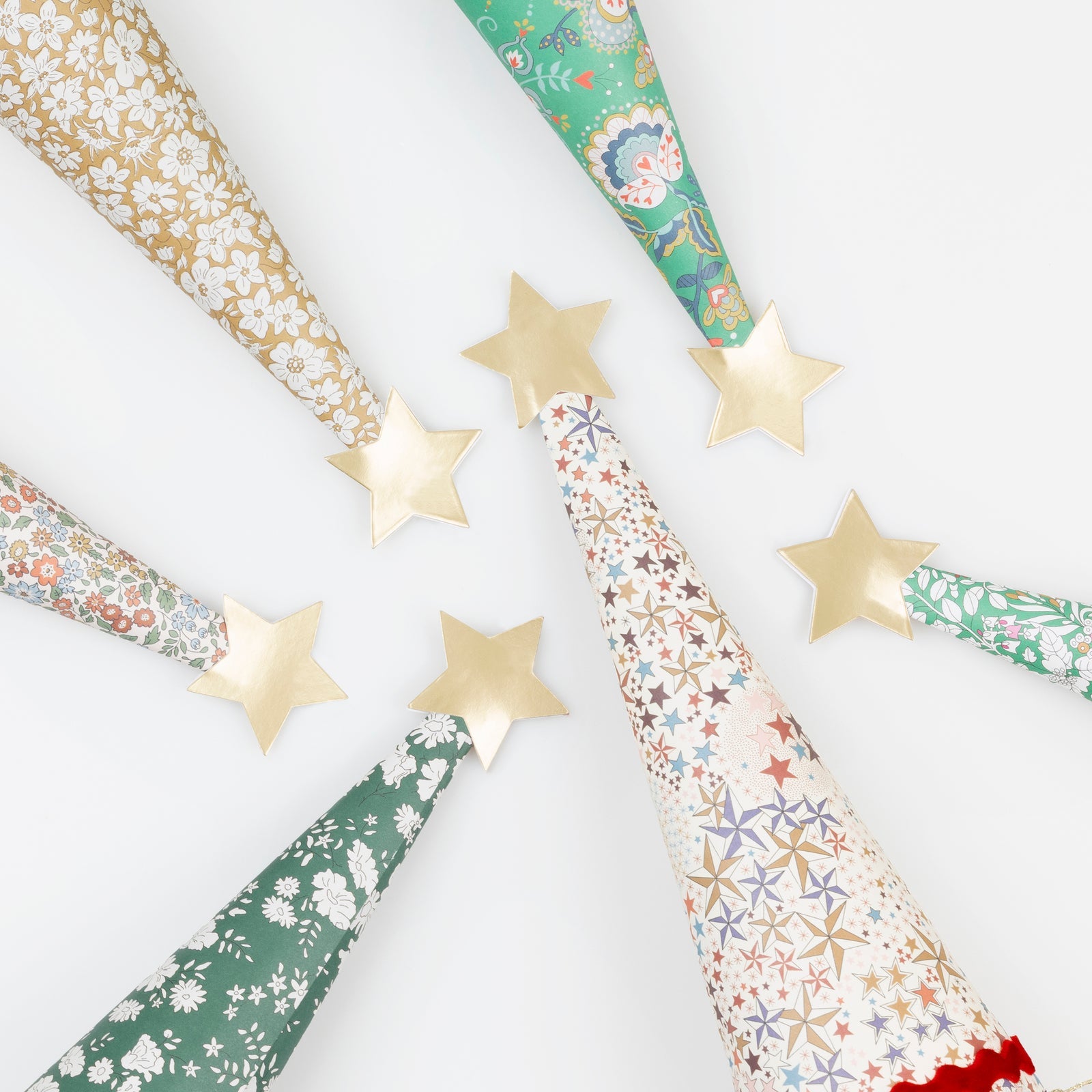 Six cone-shaped Liberty Tree Crackers by Meri Meri, featuring floral and star patterns, are arranged in a circle on a white background, each topped with a gold star and evoking festive Christmas party style.