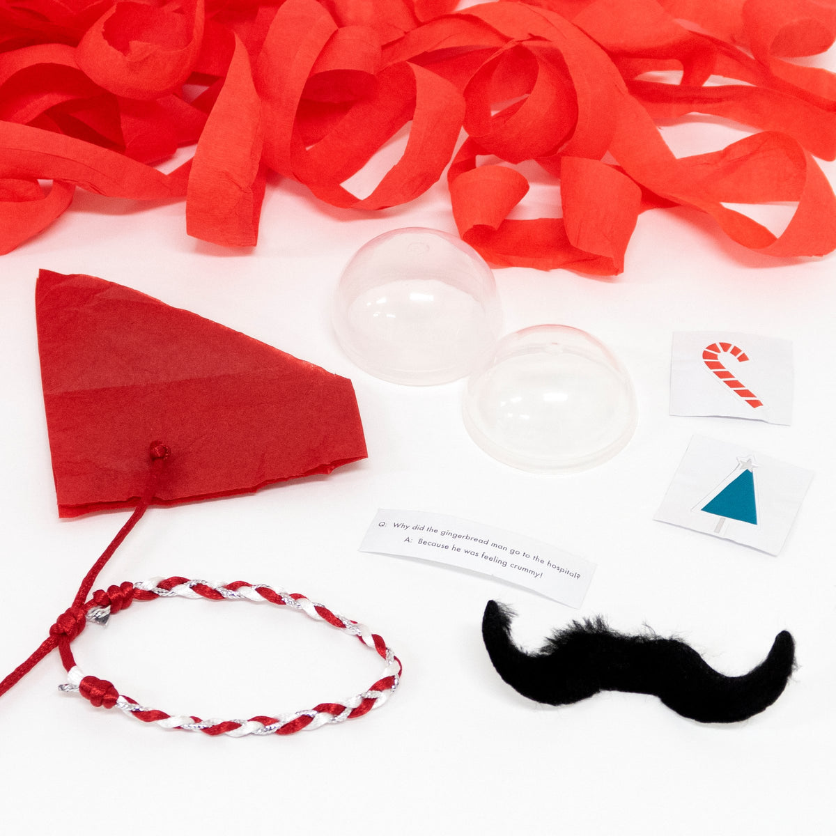 Peppermint Candy Surprise Balls by Meri Meri include red streamers, a red paper hat, plastic domes, a braided bracelet, fake mustache, printed cards, and a joke—perfect festive treats or stocking fillers for party bags. All displayed on a white surface.