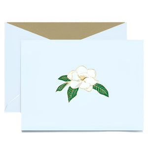 The Magnolia Blossom Classic Card Set by Crane features a light blue card with a white magnolia and green leaves, plus a matching envelope with gold interior—perfect for sending heartfelt notes symbolizing strength.
