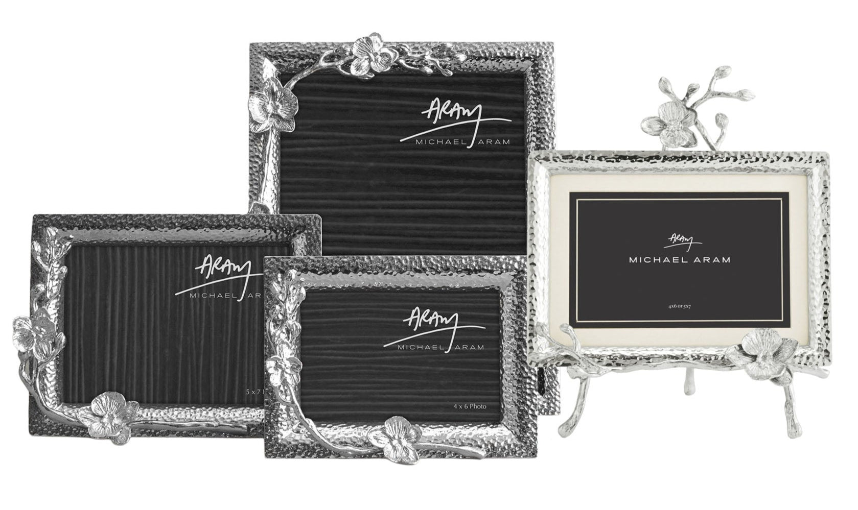 The White Orchid Frame Collection by Michael Aram features four silver photo frames with graceful orchid motifs; three are upright, and one is displayed on a decorative stand.