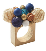 Decorative centerpiece composed of a handmade wooden stand with a circular cutout, topped with an assortment of textured spheres in blue, gold, and neutral tones featuring Kim Seybert Java Napkin Rings.