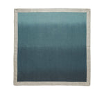 The Kim Seybert Dip Dye Napkin Set features rectangular napkins with a beige border and a blue ombre center, hand-dipped to fade from light blue at the top to dark blue at the bottom.