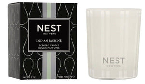 A Nest Indian Jasmine Votive Candle crafted from premium wax sits in a clear glass holder beside its decorative black and white box.