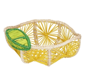 The Mercedes Salazar Lemon Basket is a woven storage basket shaped like a lemon slice, crafted in yellow and natural straw with green and yellow leaf detail—a playful addition to your space.