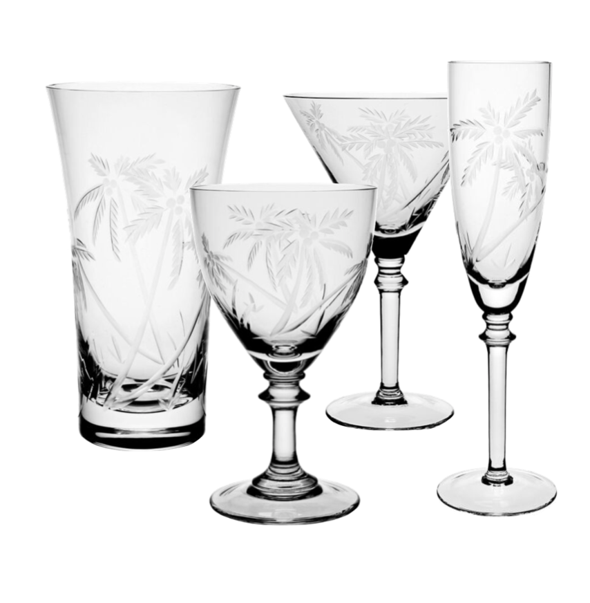 The Palmyra Drinkware Collection by William Yeoward Crystal features four etched pieces—a tumbler, wine glass, martini glass, and champagne flute—with palm tree designs inspired by Palmyra Atoll against a white background.
