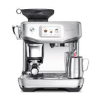 The Breville Barista Touch Impress Espresso Machine features a stainless steel design, digital display, built-in grinder, Impress Puck System, portafilter, and a steam wand frothing milk in a metal cup.