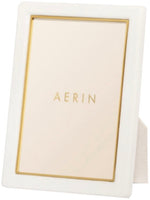 Aerin's Piero Leather Frame Collection features a white rectangular photo frame with gold detailing and a gold inner border, showcasing “AERIN” in gold at the center for an elegant display.