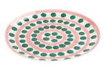 The Symi Green and Pink Dinnerware Collection by Themis Z features a handcrafted porcelain plate with a white base, adorned with pink concentric circles and green dots in the distinctive Symi pattern.