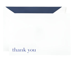 A Bodoni Thank You Folded Card from Crane, printed on Pearl White paper with blue "thank you" text, is partially tucked into a white envelope featuring a dark blue interior.