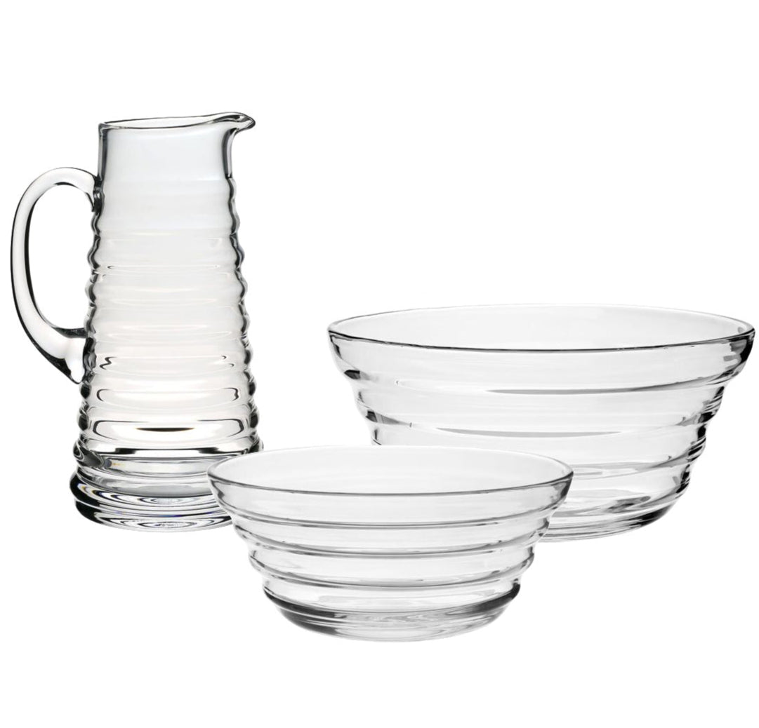 The William Yeoward Crystal Ripples Serveware Collection, featuring a clear glass pitcher and two bowls with horizontal ridges, is displayed on a white background for an artisanal touch.
