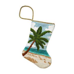 The Seaside Serenity Needle Point Stocking by Bauble Stockings features a hand-stitched beach scene with palm tree, sand, ocean, and sky, plus a gold hanging loop—ideal for coastal holiday decor.