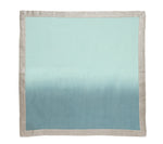 A Kim Seybert Dip Dye Napkin from the Dip Dye Napkin Set, featuring a hand-dipped light blue and teal ombre center with a beige border, is laid flat on a white background.