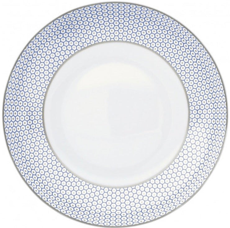 The Tresor Blue Dinnerware Collection by Raynaud features a white porcelain plate with a hand-painted blue honeycomb pattern around the rim, highlighting elegant craftsmanship.