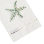 The Haute Home Starfish Bath Collection in Aqua features a white towel with a blue starfish design, hand-embroidered edges, and label. Inspired by Italian linen, it adds elegance to any space.