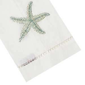 The Haute Home Starfish Bath Collection in Aqua features a white towel with a blue starfish design, hand-embroidered edges, and label. Inspired by Italian linen, it adds elegance to any space.