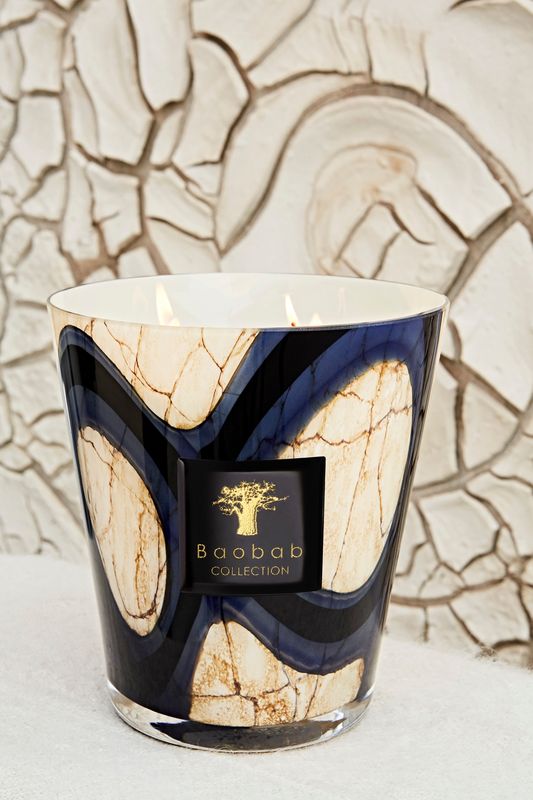 A Baobab Collection Stones Lazuli Candle from Baobab, with a blue and beige marbled design, is placed against a textured stone background, infusing the air with sea salt and musk.
