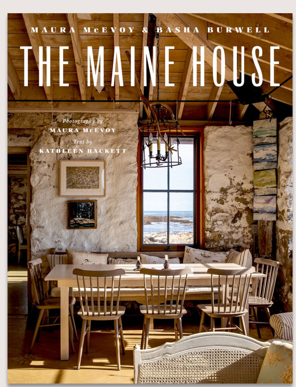 The Maine House by Abrams features a book cover with a rustic Maine dining area—wooden chairs, round table, exposed beams, stone walls, artwork, and a window with coastal views.