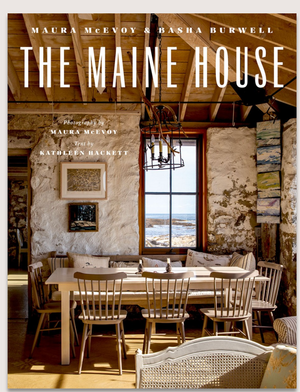 The Maine House by Abrams features a book cover with a rustic Maine dining area—wooden chairs, round table, exposed beams, stone walls, artwork, and a window with coastal views.