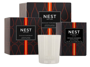 A white Nest Sicilian Tangerine Candle from the Sicilian Tangerine Candle Collection sits in front of three matching black and orange boxes.