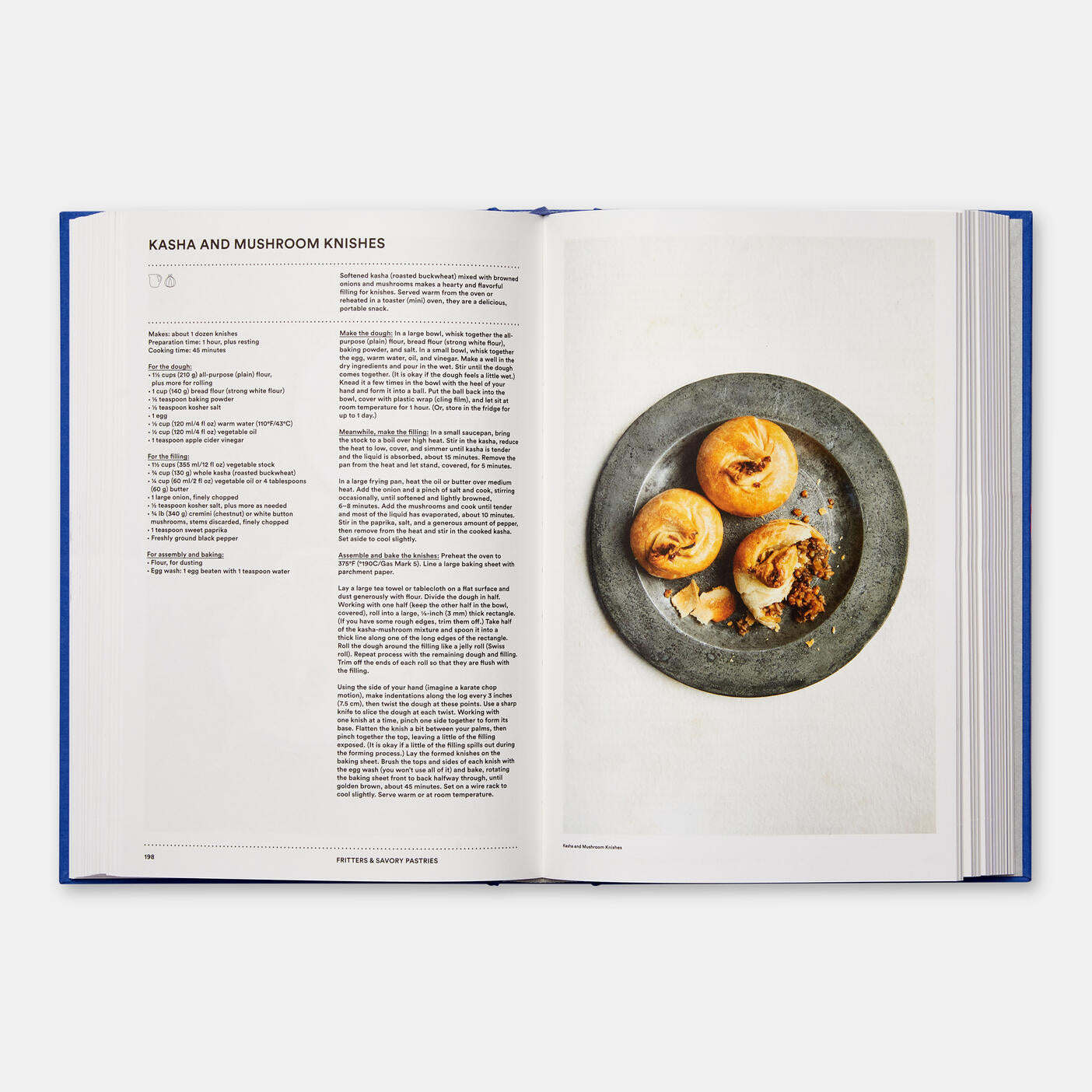 An open copy of *The Jewish Cookbook* by Phaidon highlights a recipe for "Kasha and Mushroom Knishes" on the left page, accompanied by a tempting photo of three knishes displayed on a gray plate on the right.