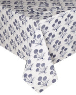 A white tablecloth from the SLOANE BY HAND Poppy Table Linen Collection showcases blue floral clusters in a hand block print-inspired pattern, elegantly draped over a rectangular table.