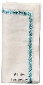 The Kim Seybert Jardin Napkin Set features folded white linen napkins with elegant turquoise embroidery along two edges, labeled "White/Turquoise.