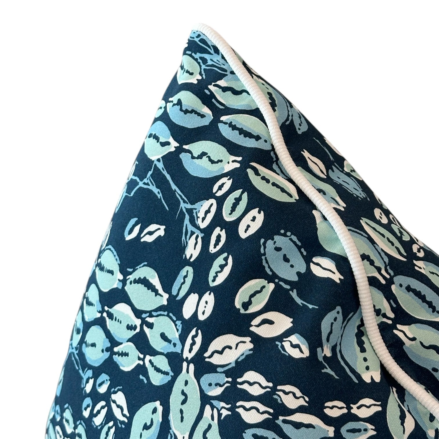 Close-up of the Cowrie Shell Navy Outdoor Pillow by Associated Design, handmade with premium materials, featuring a white piped edge and a botanical leaf pattern in navy and light blue.