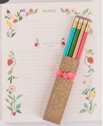 The Karen Adams Strawberry Notepad features lined pages labeled "NOTES" and comes with four colorful pencils, all in full color ink, nestled in a decorative box tied with a pink ribbon.