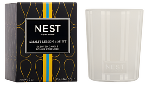 The Nest Amalfi Lemon & Mint Collection candle comes in a white jar with packaging inspired by the Amalfi Coast, featuring a black box adorned with yellow and blue accents.