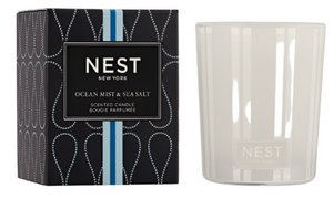 A white Nest Ocean Mist & Sea Salt Candle from the Candle Collection sits by its black and blue box, evoking the refreshing essence of ocean mist with hints of sea salt.