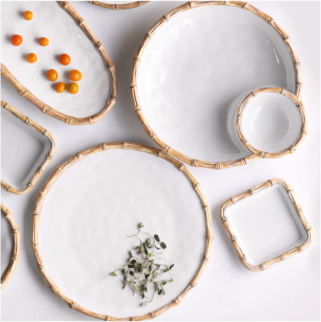 White ceramic-look dishes from the Vida Natural Bamboo Serveware Collection by Beatriz Ball, featuring bamboo-style rims, are arranged on a white surface; some hold cherry tomatoes or microgreens, while most are empty. Stylish and break-resistant melamine.