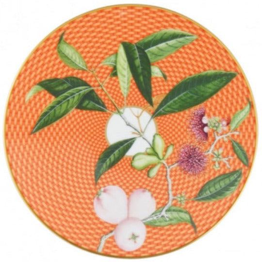 The Tresor Fleuri Orange Dinnerware Collection by Raynaud features a round orange porcelain plate with a woven pattern, hand-painted green leaves, pink and white fruits, and purple flowers on a branch.