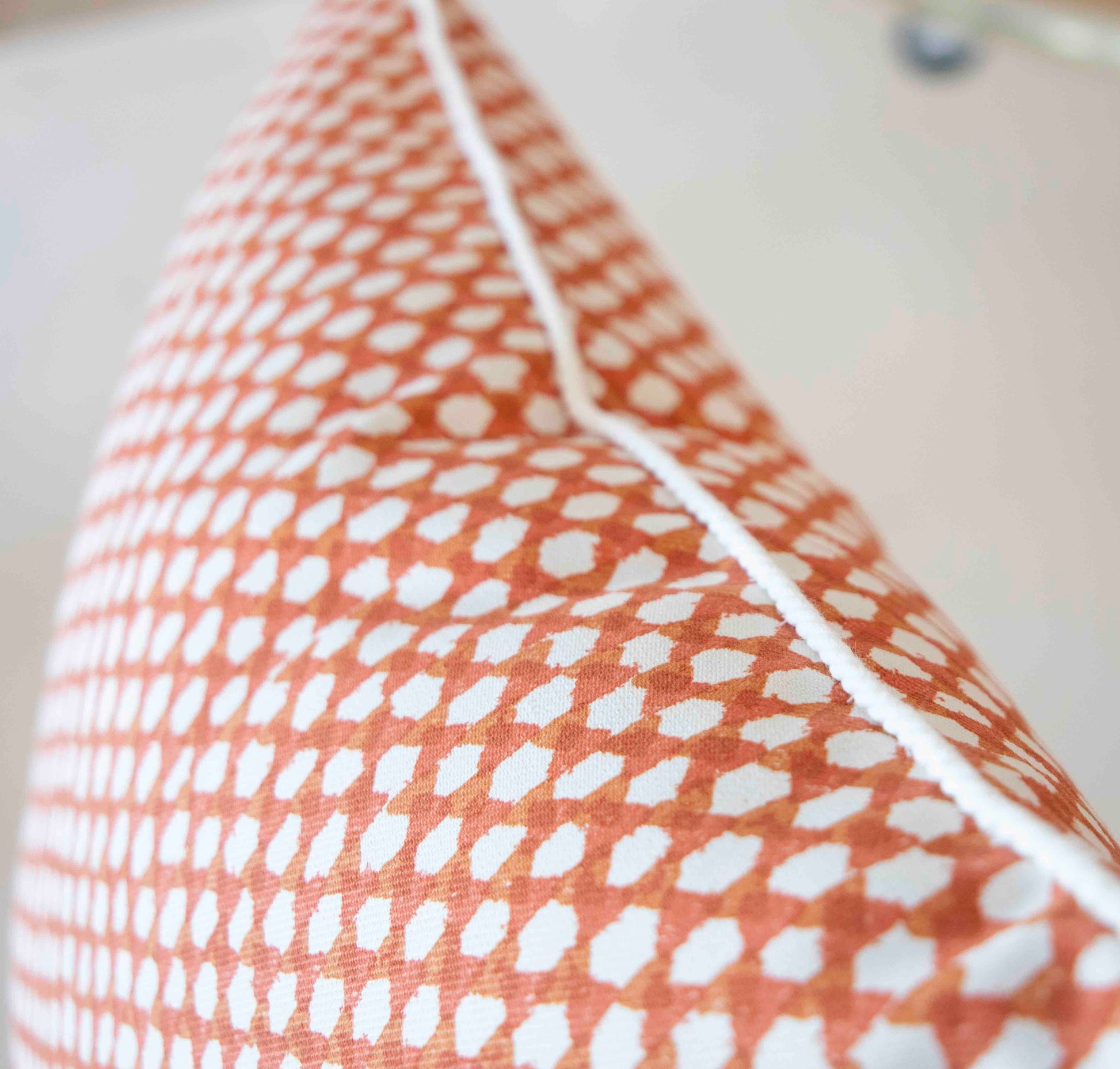 Close-up of the Associated Design Mandarin Wicker Outdoor Pillow, featuring an orange and white pattern, visible seam, and white piping along the edge, expertly crafted for outdoor elegance.