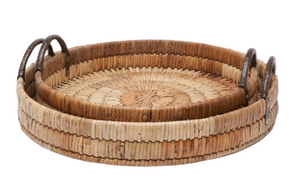The Royston Round Tray Collection by Orlebar Brown includes two nested round woven rattan trays with hammered iron handles in natural tan and brown tones.