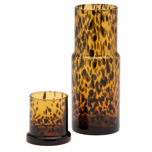 The Pigeon & Poodle Faro Tortoise Shell Carafe, tall and cylindrical with amber and black spots, sits beside a matching short tumbler, exuding refined hospitality against a plain white background.