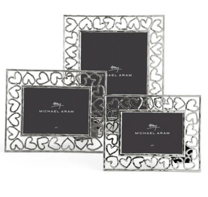The Michael Aram Heart Frame Collection includes three silver frames with heart-shaped cutouts, each featuring a central placeholder with the brand logo—a tribute to handcraftsmanship and love.