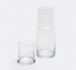 The Faro Clear Carafe by Pigeon & Poodle is placed beside an empty clear glass tumbler on a plain white background, embodying timeless hospitality.