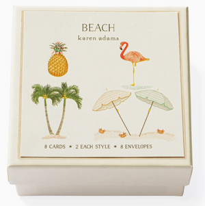 The Karen Adams Beach Gift Enclosure Set features a cream box with "BEACH" on it and hand-finished illustrations of pineapples, flamingos, palm trees, and beach umbrellas. Includes 8 cards and envelopes—a charming gift addition.