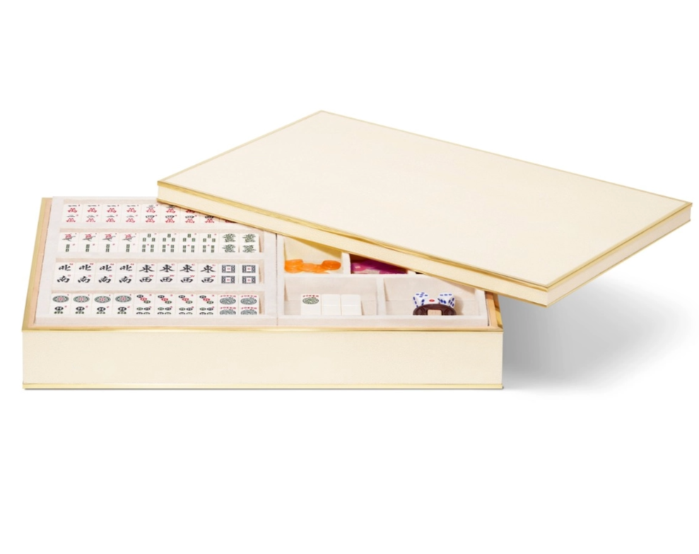 The Aerin Luxe Shagreen Mahjong Set in cream features a luxurious box with a partially open lid, revealing neatly arranged engraved tiles, dice, and playing pieces inside.