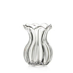The Simon Pearce Chelsea Optic Posy Vase features clear glass with a wide base, curved sides, and a scalloped rim. Ideal as an elegant housewarming gift, it stands empty against a plain white background.