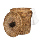 The Lamia Natural Rattan Hamper by Pigeon & Poodle features a removable lid leaning against it and a white towel draped over its edge.