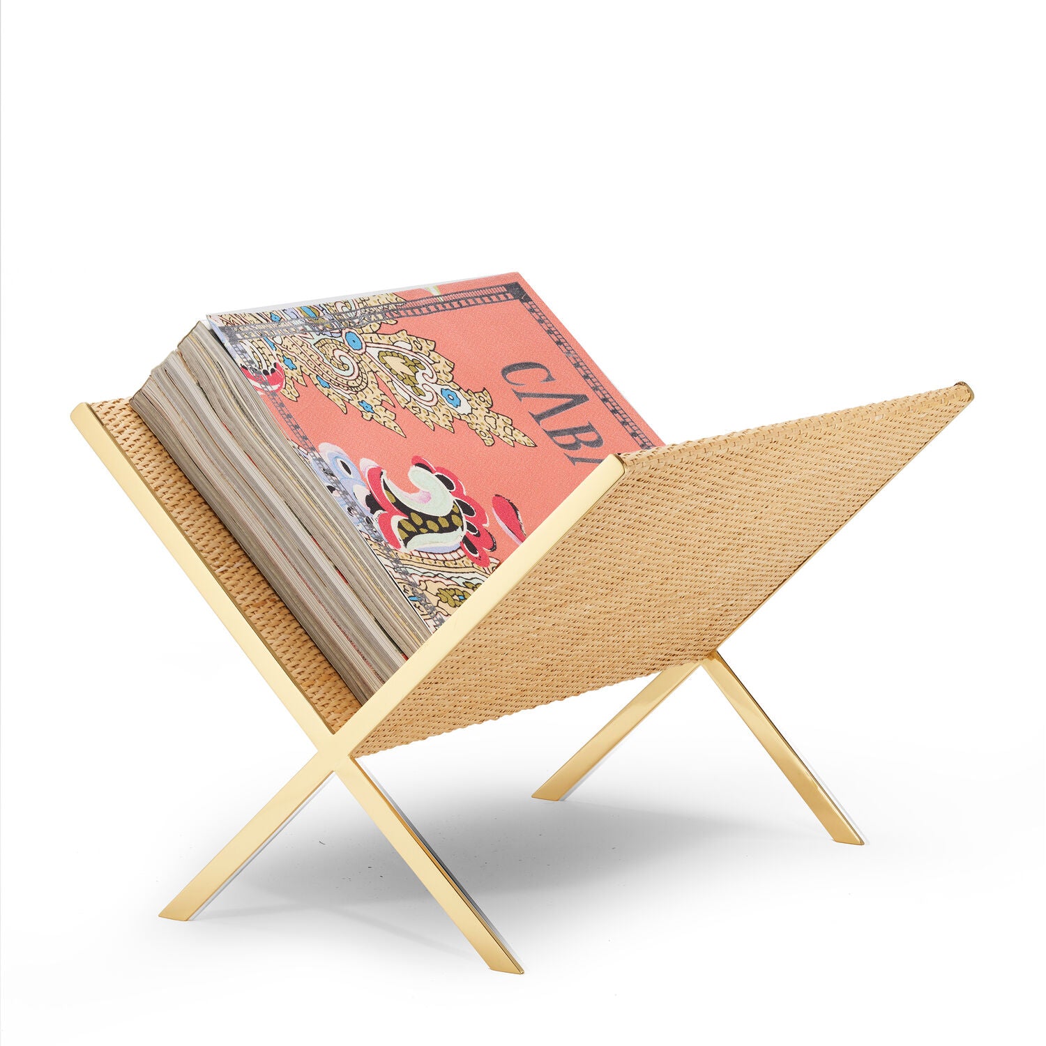 The Aerin Colette Cane Magazine Rack, featuring woven cane and brass legs, holds a vibrant "CABINETS" magazine against a white background.