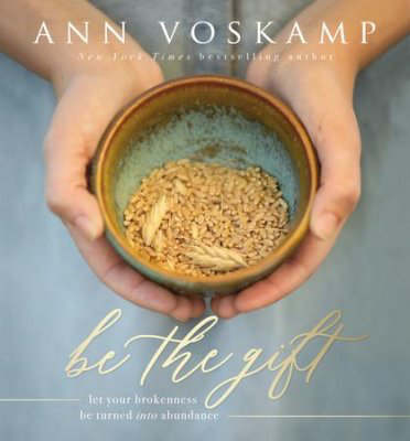 Book cover with the title "Be The Gift" by Ann Voskamp, published by Thomas Nelson, featuring hands holding a bowl with grains and highlighting transformational practices.